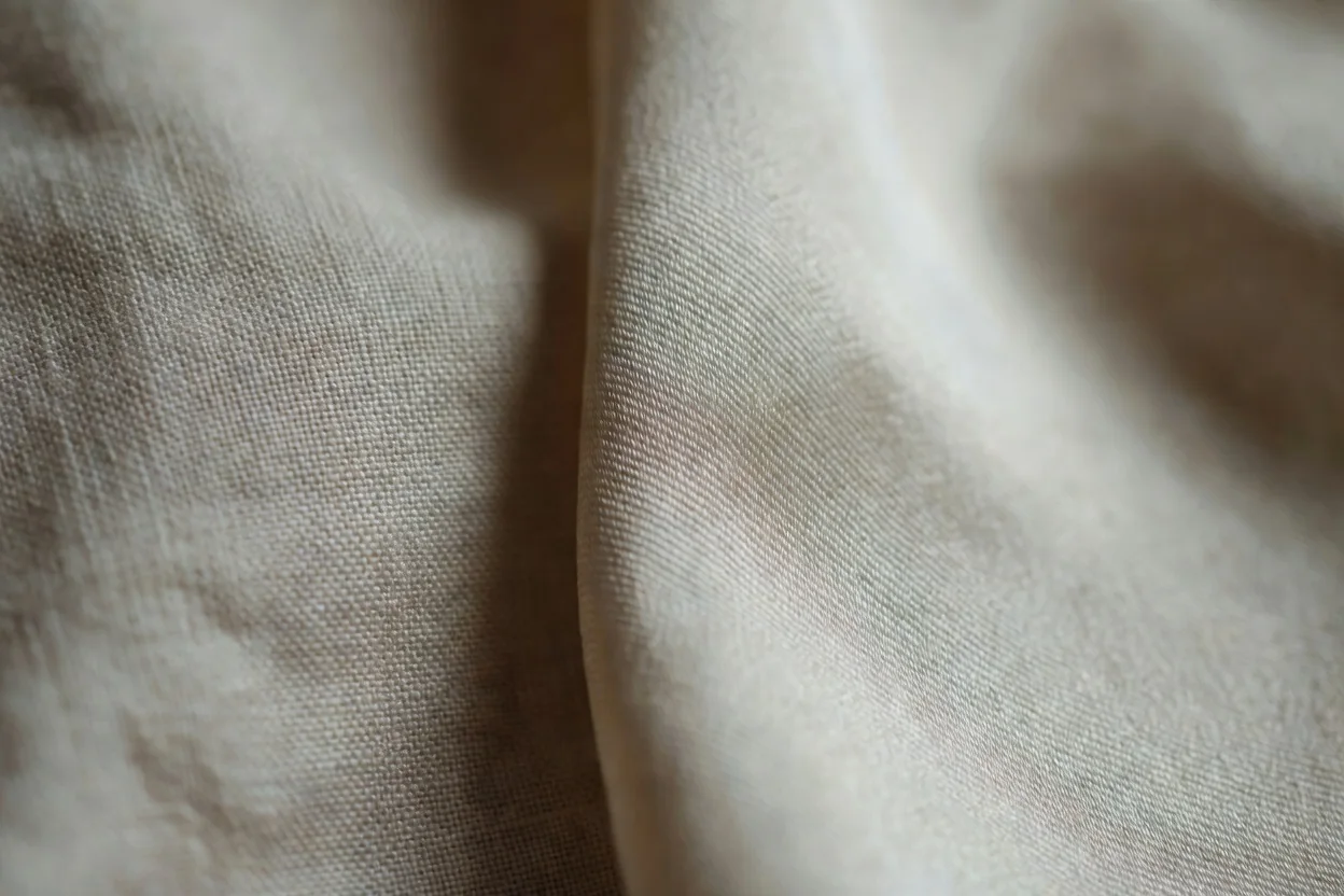 Un foulard en twill de soie écru à motif cachemire déployé en diagonal sur une table en bois